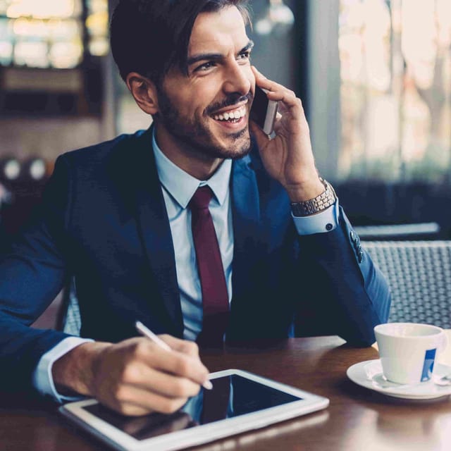 Smiling professional speaking on the phone with a tablet in hand, representing the flexibility and global reach of Berlitz teaching English jobs.

