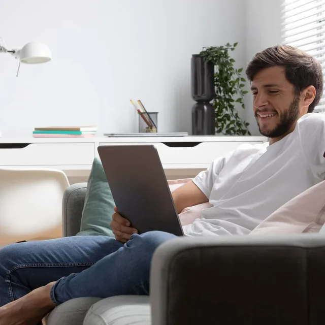 Man relaxing on a couch while using a tablet at home.