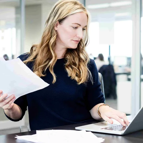 Professional reviewing documents and working on a laptop in a modern office.