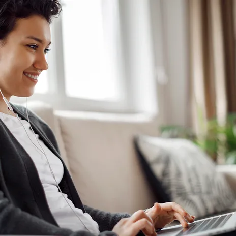 Smiling woman learning online with earphones and laptop, representing Berlitz language school's flexible remote classes.