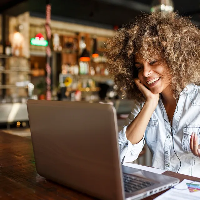 Smiling woman attending online Spanish classes for adults from a cozy café using her laptop
