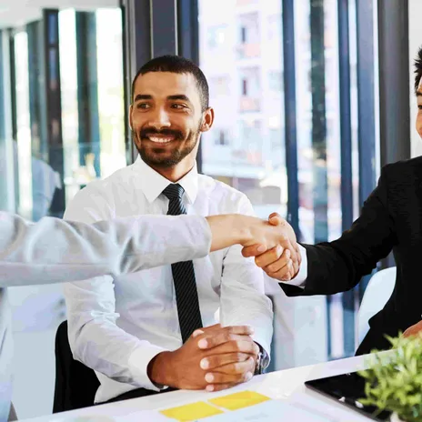 Business professionals shaking hands during a successful Berlitz corporate English training session in a modern office environment.


