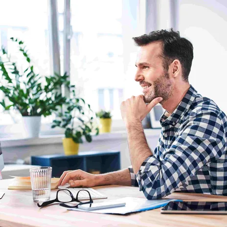 Smiling man working remotely at a desk with a computer, ideal for flexible German tutor jobs online.