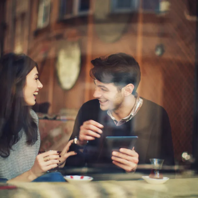 Two young adults laughing and conversing at a café, embodying Berlitz language school’s real-world language learning approach.

