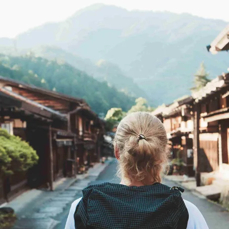 Back view of a solo traveler walking through a traditional Japanese village, symbolizing cultural immersion and language learning with Berlitz.com.
