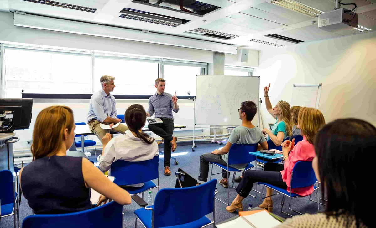 Language training session at Berlitz.com featuring adult students and instructors in an interactive classroom environment with whiteboard instruction.
