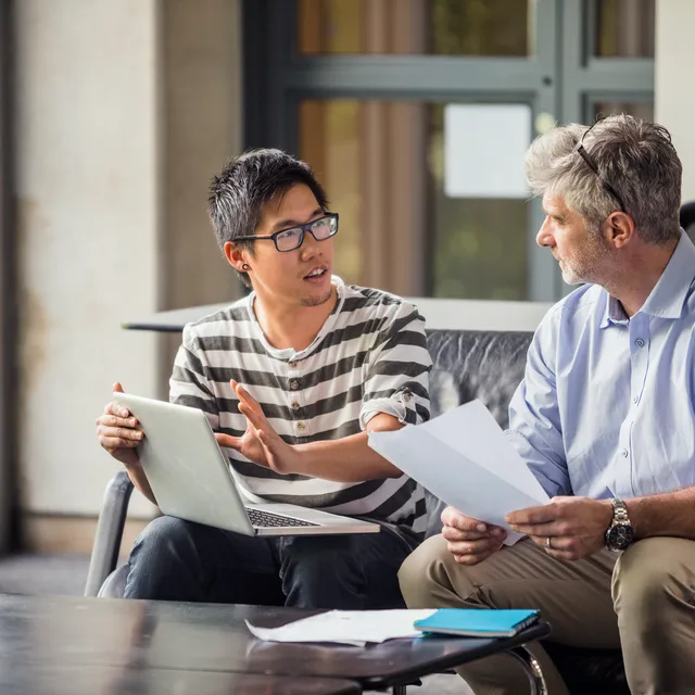 Two men engaged in a thoughtful discussion with a laptop and documents, representing mentorship and growth opportunities within Berlitz careers.